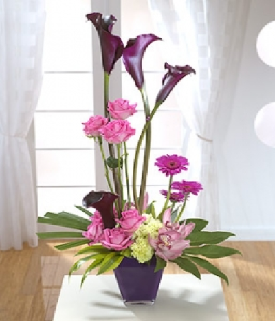 Bossa Nova - Calla Lilies stand tall above pink Roses and Gerbera with low set Carnations and exotic Cymbidium Orchid heads on palm leaves.