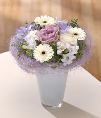 Cool Heather - A single lavender Rose is central to this vase arrangement which sits in a sisal collar with lavender Gerbera, white Carnation, Germini and scented Freesia. 