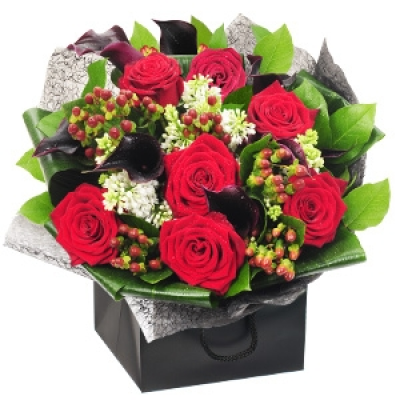Red Carpet Romance - A dramatic expression of love, Red Carpet Romance features long-stemmed grand prix roses and elegant black calla lilies with luscious hypericum berries and soft ruscus foliage. The whole bouquet is then perfectly framed with folded aspidistra and a black weave, delivered in a beautiful presentation bag. Perfect for saying 'I love you!'