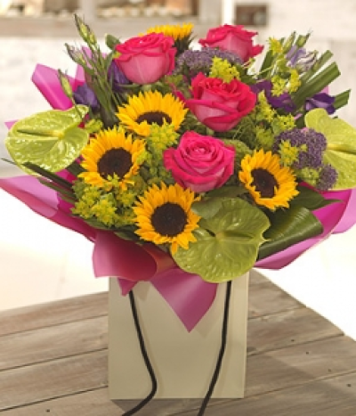 Summer Madness - This bright and cheerful hand-tied is aqua packed for freshness. Scented Roses are accompanied by bright Sunflowers, vibrant Anthuriums and delicate Lisianthus. Beautifully wrapped and presented in a gift bag.