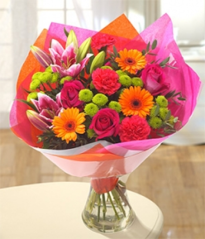 Rainbow - Delight the senses with this fantastically vibrant and fragrant bouquet. Orange Germini, cerise Roses and Carnations have been perfectly married with gorgeous green Santini and Cobra Lilies.