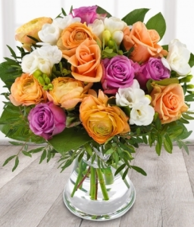 Coral Bouquet - A modern classic made with the most gorgeous cerise roses, peach roses, peach ranunculus and white freesia, finished with mixed foliage. Available during Spring
