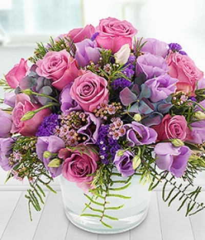 Chateau - An incredible mix of beautiful blue Hydrangeas, pretty pink Roses & Wax Flowers, lilac Lisianthus, purple Statice and just a dash of Rosemary, expertly arranged in a pretty pastel blue glass pot.
