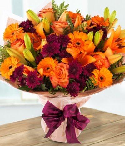 Autumn Sun - A sumptuous autumnal bouquet inspired by the colours of the season. Deep burgundy Spray Chrysanthemums sit perfectly amongst a glorious display of orange Roses, Lilies and Germinis.